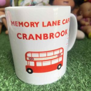 แก้วมัคใบนี้มีข้อความ “MEMORY LANE CAFE CRANBROOK” และรูปภาพรถบัสสองชั้นสีแดง